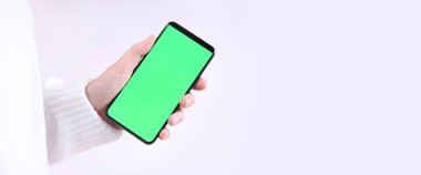 Yeşil ekranlı cep telefonu. Yeşil ekranlı akıllı telefonu tutan kadın eller, yakın plan. Beyaz arka planda telefonu olan beyaz kazaklı bir kız. Kromakey cep telefonunu tutan tanımlanamayan el