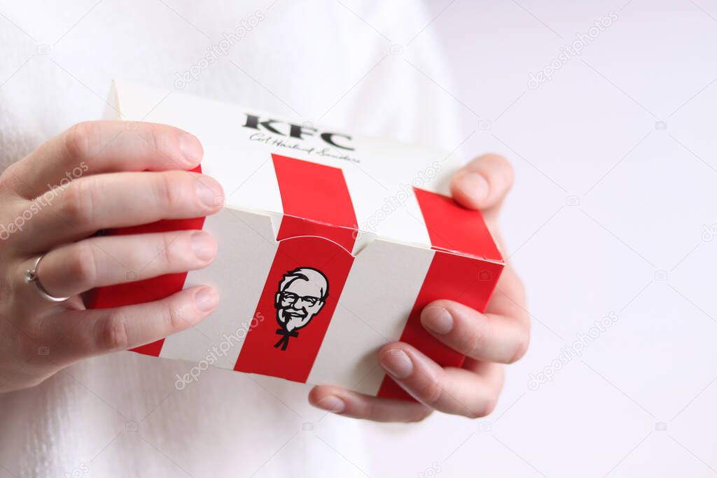 Kyiv, Ukraine - December 15, 2024: Cardboard box with food from KFC fast food. Popular fast food chain - Kentucky Fried Chicken. Female hands holding KFC cardboard box, close-up, light background