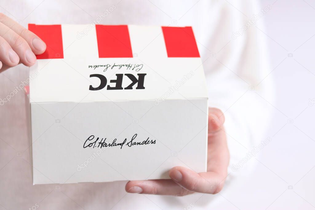 Kyiv, Ukraine - December 15, 2024: Cardboard box with food from KFC fast food. Popular fast food chain - Kentucky Fried Chicken. Female hands holding KFC cardboard box, close-up, light background
