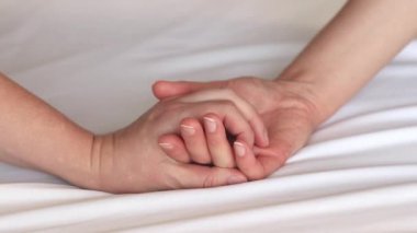 Eşcinsel ilişkiler, lezbiyenler. Eşcinsel evlilik ve aşk kavramı. Mutlu lezbiyen çift. Beyaz çarşaflar üzerinde birbirine dokunan iki kadın eli. Yatakta iki kadın eli var. Yakın plan. LGBTQ