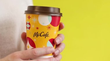 Kyiv, Ukrayna - 19 Aralık 2024: McDonalds 'dan Noel kahvesi. Elinde kahve ya da çay tutan beyaz kazaklı bir kadın. McDonald 's fast food restoranı. Sarı arka planda McCafe içkisi
