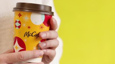 Kyiv, Ukrayna - 19 Aralık 2024: McDonalds 'dan Noel kahvesi. Elinde kahve ya da çay tutan beyaz kazaklı bir kadın. McDonald 's fast food restoranı. Sarı arka planda McCafe içkisi