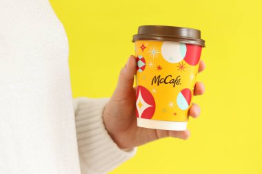 Kyiv, Ukrayna - 19 Aralık 2024: McDonalds 'dan Noel kahvesi. Elinde kahve ya da çay tutan beyaz kazaklı bir kadın. McDonald 's fast food restoranı. Sarı arka planda McCafe içkisi