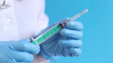 Şırıngalı hemşire ya da doktor, mavi arkaplan. Lateks eldivenli kadın elinin elinde şırınga var. Şırıngalı hemşire ya da doktor, yakın plan. Aşılama. Enjeksiyon. İlaç.