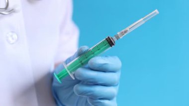 Şırıngalı hemşire ya da doktor, mavi arkaplan. Lateks eldivenli kadın elinin elinde şırınga var. Şırıngalı hemşire ya da doktor, yakın plan. Aşılama. Enjeksiyon. İlaç.