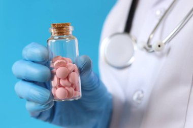 Cam şişedeki pembe haplar. Mavi arka planda bir hemşirenin ya da doktorun elindeki vitaminler. Vitaminler ve diyet takviyeleri yakın çekim. Tıbbi eldivenli doktor bir kavanoz vitamin tutuyor. İlaç.