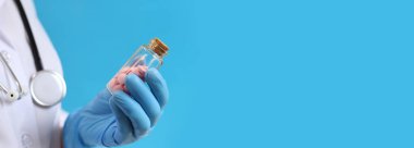 Cam şişedeki pembe haplar. Mavi arka planda bir hemşirenin ya da doktorun elindeki vitaminler. Vitaminler ve diyet takviyeleri yakın çekim. Tıbbi eldivenli doktor bir kavanoz vitamin tutuyor. İlaç.