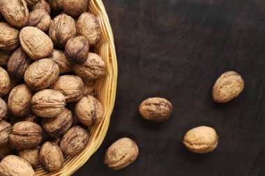 Hasır bir sepetin içindeki cevizler koyu ahşap bir arka planda. Yuvarlak bir sepette fındıklar, üst manzara. Kabuklu ceviz yığını, yakın plan, arka plan. Sağlıklı beslenme. Hasat, tarım.