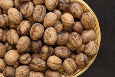 Hasır bir sepetin içindeki cevizler koyu ahşap bir arka planda. Yuvarlak bir sepette fındıklar, üst manzara. Kabuklu ceviz yığını, yakın plan, arka plan. Sağlıklı beslenme. Hasat, tarım.