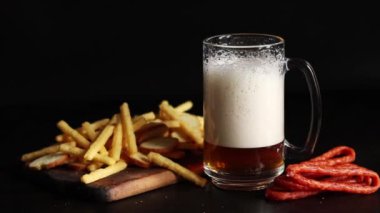 Hafif bira ve koyu arkaplanda atıştırmalıklar. Bira, patates kızartması ve av sosisi. Tahtada cam ve aperatifler. Hafif bira ve kızarmış ekmek. Geleneksel cam bira kupası.