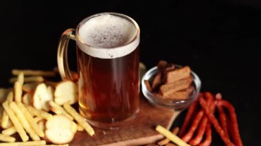 Hafif bira ve koyu arkaplanda atıştırmalıklar. Bira, patates kızartması ve av sosisi. Tahtada cam ve aperatifler. Hafif bira ve kızarmış ekmek. Geleneksel cam bira kupası.