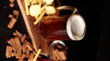 Hafif bira ve koyu arkaplanda atıştırmalıklar. Bira, patates kızartması ve av sosisi. Tahtada cam ve aperatifler. Hafif bira ve kızarmış ekmek. Geleneksel cam bira kupası.