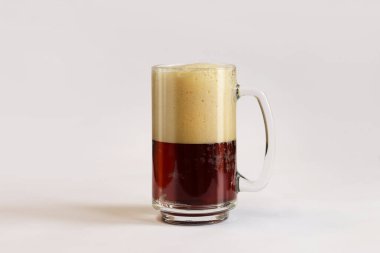 Bardakta kvass, hafif arka plan. Bir bardak koyu bira ya da açık gri arka planda köpüklü kvass. Saplı geleneksel bira bardağı. Soğuk bir içecekle bardağa yaklaş.
