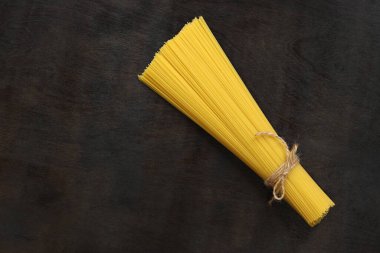 Koyu tahta arka planda çiğ spagetti. Buğdaydan spagetti. Kuru spagetti, iplikle bağlanmış, üst manzara, kopyalama alanı. Pişmemiş sarı makarna. Bir yığın spagetti, siyah masada çiğ İtalyan makarnası.