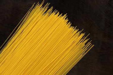 Koyu tahta arka planda çiğ spagetti. Durum buğday spagettisi. Kuru spagetti, üst manzara. Pişmemiş sarı makarna. Bir yığın spagetti, siyah masada çiğ İtalyan makarnası.