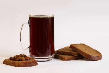 Bir kupa lezzetli kvass, hafif arka planda ekmek ve kuru üzüm. Cam bardak kvass köpüklü, yakın plan. Beyaz arka planda malzemeleri olan Kvass. Ekmek dilimleriyle taze içecek, seçici odaklanma.