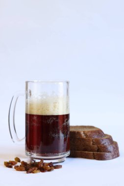 Bir kupa lezzetli kvass, hafif arka planda ekmek ve kuru üzüm. Cam bardak kvass köpüklü, yakın plan. Beyaz arka planda malzemeleri olan Kvass. Ekmek dilimleriyle taze içecek, seçici odaklanma.