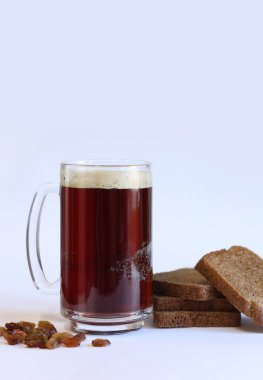 Bir kupa lezzetli kvass, hafif arka planda ekmek ve kuru üzüm. Cam bardak kvass köpüklü, yakın plan. Beyaz arka planda malzemeleri olan Kvass. Ekmek dilimleriyle taze içecek, seçici odaklanma.