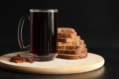 Esmer arka planda bir kupa lezzetli kvass, ekmek ve kuru üzüm. Ahşap bir tahtanın üzerinde cam bir bardak kvass, yakın plan. Siyah arka planda malzemeler olan koyu kvass. Dilimlenmiş ekmekle taze içecek.