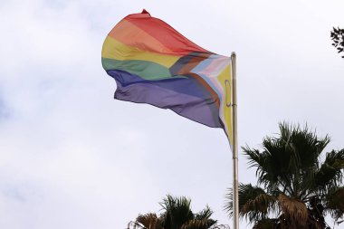 Salou, Spain - September 18, 2024: Intersex-inclusive redesign of the Progress Pride Flag. Rainbow LGBT flag against the sky. Flag flutters in the wind in bad weather clipart