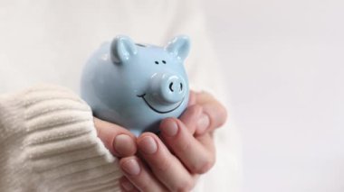 Domuz kumbarası kadınların elinde, yakın plan. Mavi domuz kumbarası, tasarruf ve finansal planlama kavramı. Kumbarası olan kazaklı bir kadın gelecek için para topluyor. Şirin domuz kumbarasının yakın çekimi.