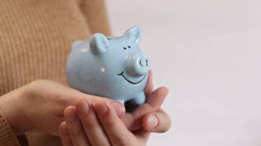 Domuz kumbarası kadınların elinde, yakın plan. Mavi domuz kumbarası, tasarruf ve finansal planlama kavramı. Kumbarası olan kazaklı bir kadın gelecek için para topluyor. Şirin domuz kumbarasının yakın çekimi.