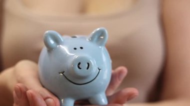 Domuz kumbarası kadınların elinde, yakın plan. Mavi domuz kumbarası, tasarruf ve finansal planlama kavramı. Kumbaralı bir kadın, gelecek için para topluyor. Şirin mavi domuz kumbarasının yakın çekimi