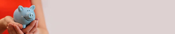 Свинка в женских руках с копировальным местом. Голубая копилка, концепция экономии денег и финансового планирования. Женщина в красной футболке с копилкой на светлом фоне. Милая голубая копилка. Баннер