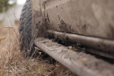 Çamurda kamyonet, off-road lastikleri, yakın plan. Toprak yolda araba tekerleği, kuru çimenler. Kamyonetin kenarına çamur sıçramış. Macera, sonbaharda açık havada. Off-road aracı, macera. Kamyonet basamağı.