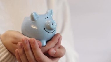 Domuz kumbarası kadınların elinde, yakın plan. Mavi domuz kumbarası, tasarruf ve finansal planlama kavramı. Kumbarası olan kazaklı bir kadın gelecek için para topluyor. Şirin domuz kumbarasının yakın çekimi.