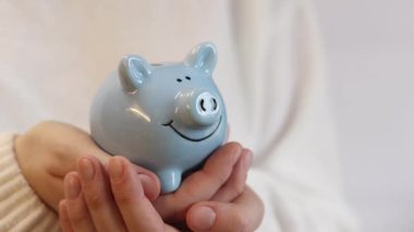 Domuz kumbarası kadınların elinde, yakın plan. Mavi domuz kumbarası, tasarruf ve finansal planlama kavramı. Kumbarası olan kazaklı bir kadın gelecek için para topluyor. Şirin domuz kumbarasının yakın çekimi.