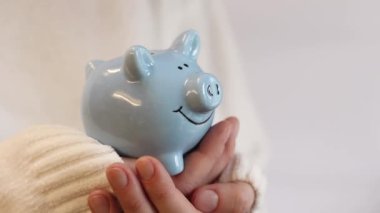 Domuz kumbarası kadınların elinde, yakın plan. Mavi domuz kumbarası, tasarruf ve finansal planlama kavramı. Kumbarası olan kazaklı bir kadın gelecek için para topluyor. Şirin domuz kumbarasının yakın çekimi.