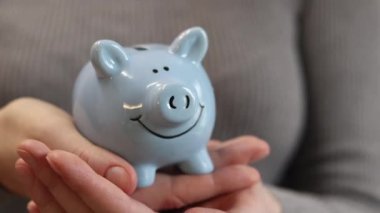 Domuz kumbarası kadınların elinde, yakın plan. Mavi domuz kumbarası, tasarruf ve finansal planlama kavramı. Kumbarası olan kazaklı bir kadın gelecek için para topluyor. Şirin domuz kumbarasının yakın çekimi.