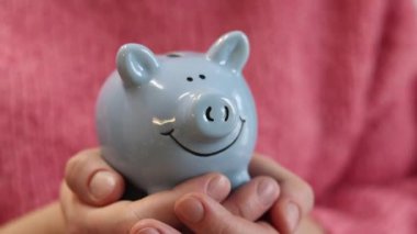 Pembe, sıcak kazaklı bir kadın kumbarayı elinde tutuyor, yakın plan. Domuz kumbarası kadınların elinde. Mavi domuz kumbarası, tasarruf ve finansal planlama kavramı. Şirin domuz kumbarasının yakın çekimi.