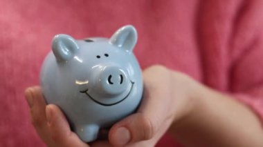 Pembe, sıcak kazaklı bir kadın kumbarayı elinde tutuyor, yakın plan. Domuz kumbarası kadınların elinde. Mavi domuz kumbarası, tasarruf ve finansal planlama kavramı. Şirin domuz kumbarasının yakın çekimi.