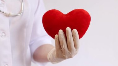 Kalp bir doktorun ellerindedir. Bir kardiyologun ellerinde yumuşak bir kalp. Tıbbi eldiven giymiş bir doktorun elinde oyuncak kırmızı bir kalp bulunur. Kalp atışını taklit eder, yakın plan. Nabız