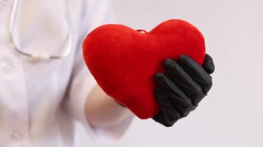 Kalp bir doktorun ellerindedir. Bir kardiyologun ellerinde yumuşak bir kalp. Tıbbi eldiven giymiş bir doktorun elinde oyuncak kırmızı bir kalp bulunur. Kalp atışını taklit eder, yakın plan. Nabız