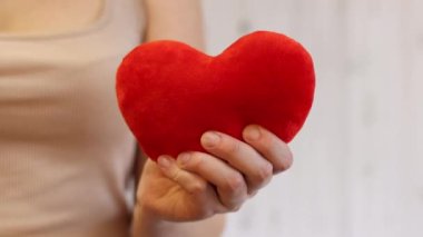 Oyuncak kalp kızın ellerinde. Yumuşak yumuşak bir kalp kadının ellerinde, yakın plan. Sevgililer Günü hediyesi, aşkın sembolü. Duygular ve ruh hali. Aşkın sembolü olarak kalp. Oyuncak kırmızı yumuşak kalp