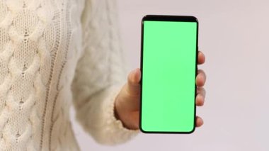 Telefonu yeşil ekran ile tutuyor. Kadın akıllı telefonu elinde tutuyor. Modern aletler. Cep telefonunun yakın çekimi. Krom anahtar, internette sörf, içeriği görmek. Yeşil ekranlı akıllı telefon