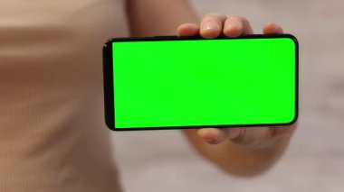 Telefonu yeşil ekran ile tutuyor. Kadın akıllı telefonu elinde tutuyor. Modern aletler. Cep telefonunun yakın çekimi. Krom anahtar, internette sörf, içeriği görmek. Yeşil ekranlı akıllı telefon