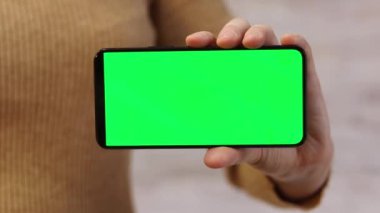 Telefonu yeşil ekran ile tutuyor. Kadın akıllı telefonu elinde tutuyor. Modern aletler. Cep telefonunun yakın çekimi. Krom anahtar, internette sörf, içeriği görmek. Yeşil ekranlı akıllı telefon