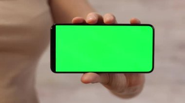 Telefonu yeşil ekran ile tutuyor. Kadın akıllı telefonu elinde tutuyor. Modern aletler. Cep telefonunun yakın çekimi. Krom anahtar, internette sörf, içeriği görmek. Yeşil ekranlı akıllı telefon