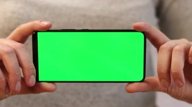 Telefonu yeşil ekran ile tutuyor. Kadın akıllı telefonu elinde tutuyor. Modern aletler. Cep telefonunun yakın çekimi. Krom anahtar, internette sörf, içeriği görmek. Yeşil ekranlı akıllı telefon
