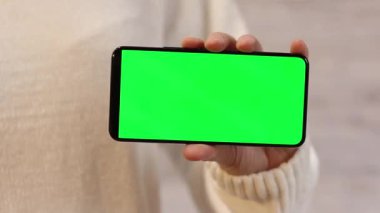 Telefonu yeşil ekran ile tutuyor. Kadın akıllı telefonu elinde tutuyor. Modern aletler. Cep telefonunun yakın çekimi. Krom anahtar, internette sörf, içeriği görmek. Yeşil ekranlı akıllı telefon