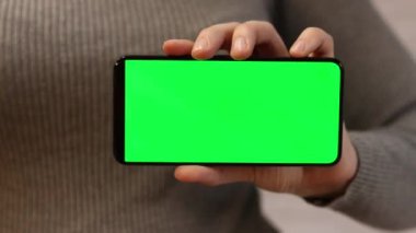 Telefonu yeşil ekran ile tutuyor. Kadın akıllı telefonu elinde tutuyor. Modern aletler. Cep telefonunun yakın çekimi. Krom anahtar, internette sörf, içeriği görmek. Yeşil ekranlı akıllı telefon