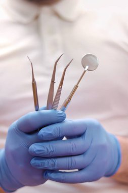 Diş aynası, cımbız ve doktor elinde sonda kancası. Dişçi konsepti. Diş hekiminde hastanın ağız boşluğunu incelemek için aletler var. Tıbbi eldivenlerdeki eller diş aletlerini tutuyor.