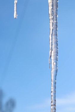 Buz saçağı gökyüzüne karşı fotoğraflandı. Seçici odaklı uzun buz sarkıtı. Kış. Soğuk bir hava. Kışın donmuş buz saçakları, yakın plan.