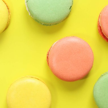 Sarı arka planda parlak Fransız badem kurabiyeleri, üst manzara. Farklı aromalı çok renkli badem kurabiyesi çeşitleri. Lezzetli hamur işleri, düz yatak. Yemek arkaplanı. Tatlılar