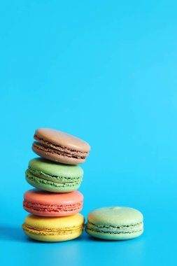 Çok sayıda renkli badem kurabiyesi yakından çekilmiş. Mavi arka planda parlak Fransız badem kurabiyeleri, yan manzara. Farklı aromalı makaron çeşitleri. Lezzetli hamur işleri, kurabiyeler, yemek geçmişi. Bir yığın tatlı.