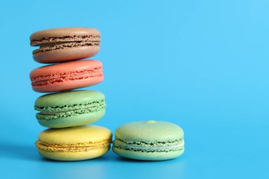 Çok sayıda renkli badem kurabiyesi yakından çekilmiş. Mavi arka planda parlak Fransız badem kurabiyeleri, yan manzara. Farklı aromalı makaron çeşitleri. Lezzetli hamur işleri, kurabiyeler, yemek geçmişi. Bir yığın tatlı.